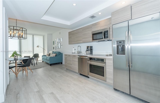 kitchen with sink, hanging light fixtures, light hardwood / wood-style floors, a chandelier, and appliances with stainless steel finishes