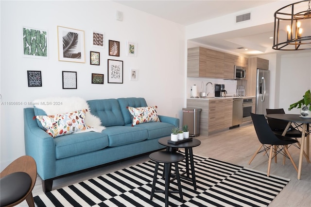 living room with sink, a chandelier, and light wood-type flooring