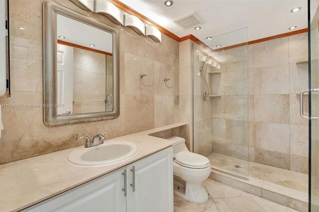 bathroom with a shower with door, vanity, toilet, and tile walls