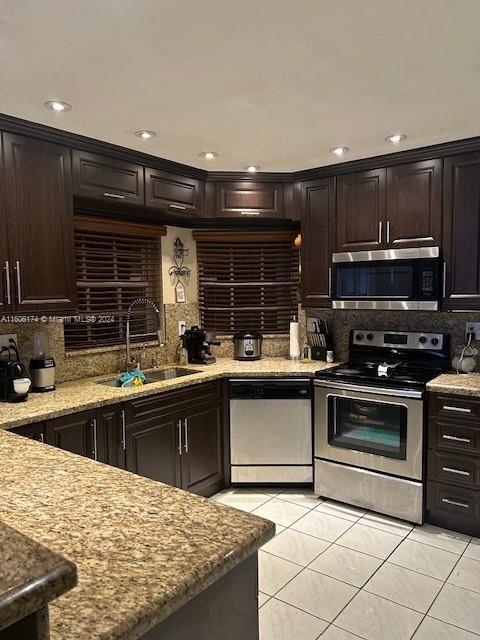 kitchen with light stone countertops, appliances with stainless steel finishes, dark brown cabinetry, sink, and light tile patterned floors