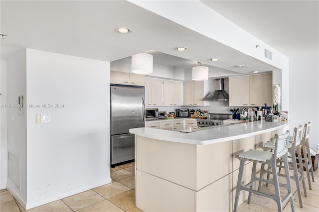 kitchen featuring wall chimney range hood, sink, appliances with stainless steel finishes, a kitchen bar, and kitchen peninsula