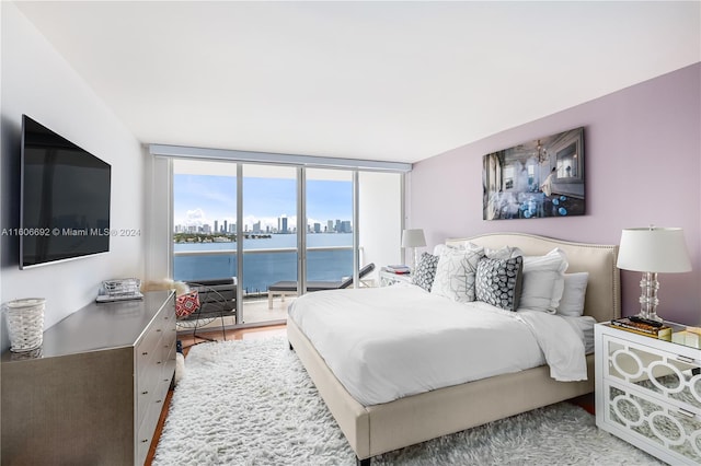 bedroom with access to exterior, a water view, a wall of windows, and hardwood / wood-style flooring