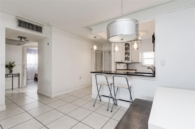 kitchen with pendant lighting, light tile patterned floors, crown molding, white cabinetry, and kitchen peninsula