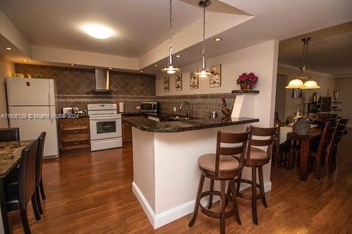 kitchen featuring white refrigerator, dark wood-type flooring, dark stone countertops, stove, and wall chimney range hood