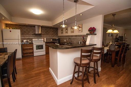 kitchen featuring dark hardwood / wood-style floors, a kitchen bar, pendant lighting, and white appliances