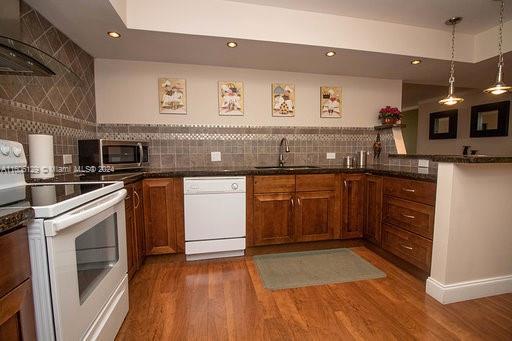 kitchen with kitchen peninsula, backsplash, wood-type flooring, sink, and white appliances