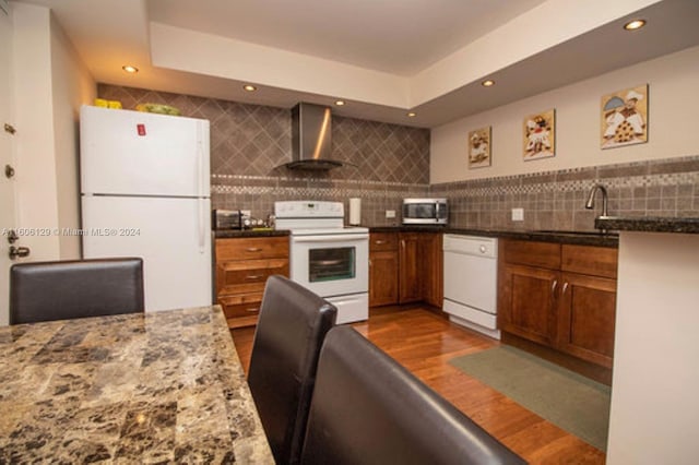 kitchen featuring white appliances, wood-type flooring, backsplash, wall chimney exhaust hood, and sink