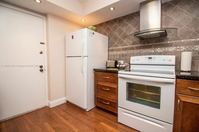 kitchen with hardwood / wood-style floors, white appliances, wall chimney range hood, and tasteful backsplash