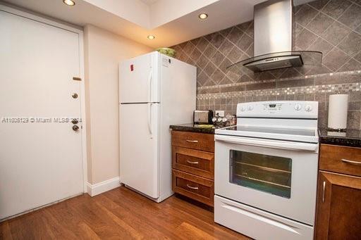 kitchen featuring tasteful backsplash, white appliances, wood-type flooring, and wall chimney exhaust hood