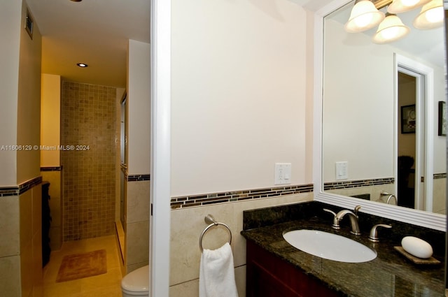 bathroom with tile floors, tile walls, a shower with door, vanity, and toilet