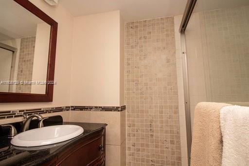 bathroom with backsplash, vanity, tile walls, and a shower with door