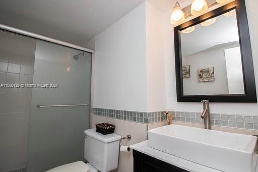 bathroom with walk in shower, vanity, toilet, and tile walls