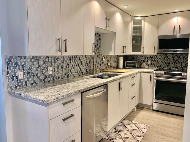 kitchen with light stone countertops, tasteful backsplash, light wood-type flooring, sink, and appliances with stainless steel finishes