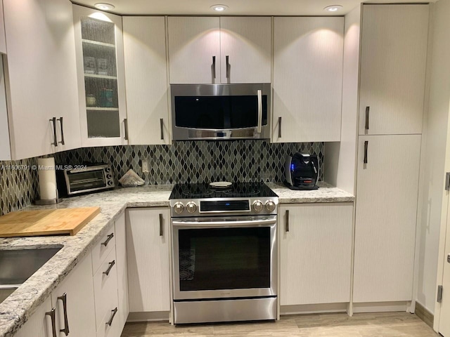 kitchen featuring appliances with stainless steel finishes, tasteful backsplash, light wood-type flooring, and light stone counters