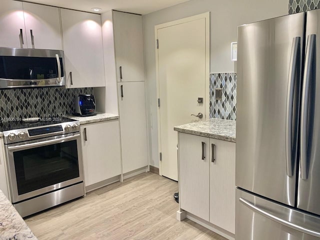 kitchen featuring appliances with stainless steel finishes, light hardwood / wood-style floors, light stone countertops, and tasteful backsplash