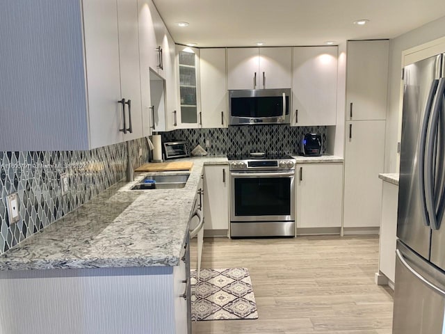 kitchen featuring stainless steel appliances, tasteful backsplash, light stone countertops, light wood-type flooring, and sink