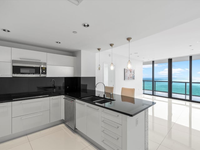 kitchen featuring stainless steel appliances, sink, a water view, a wall of windows, and white cabinets