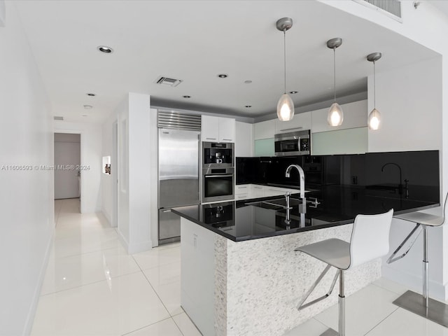 kitchen featuring kitchen peninsula, appliances with stainless steel finishes, light tile patterned floors, decorative light fixtures, and white cabinets