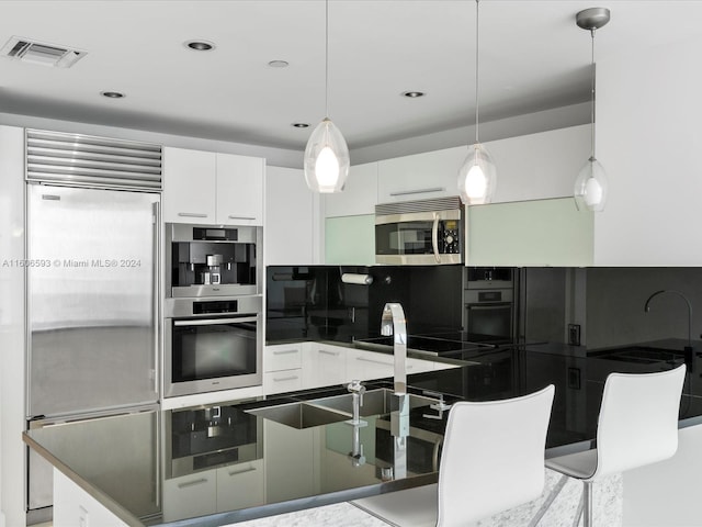 kitchen with a breakfast bar, appliances with stainless steel finishes, decorative light fixtures, and white cabinetry