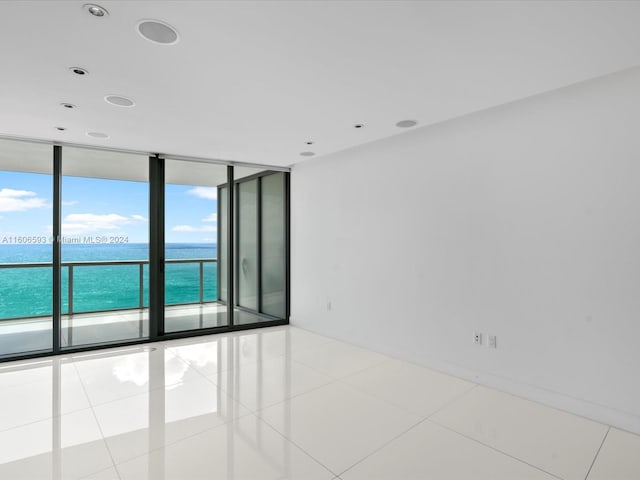 tiled empty room featuring a water view and expansive windows