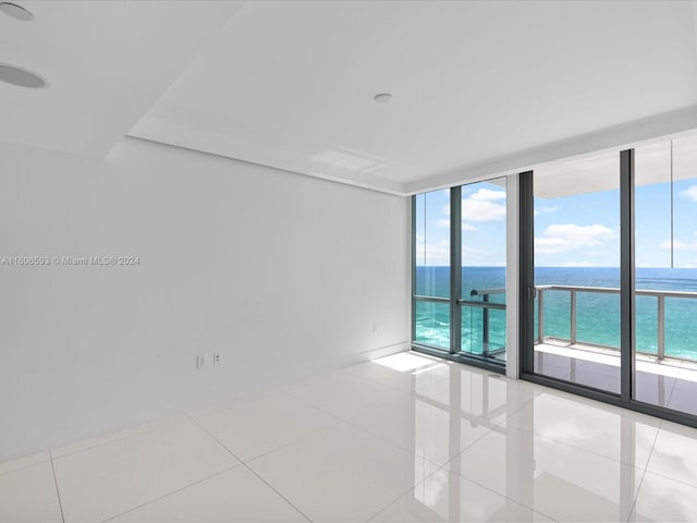 tiled empty room featuring floor to ceiling windows, plenty of natural light, and a water view