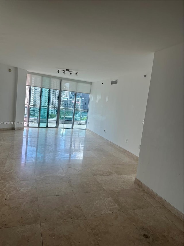 unfurnished room featuring track lighting, baseboards, visible vents, and a wall of windows