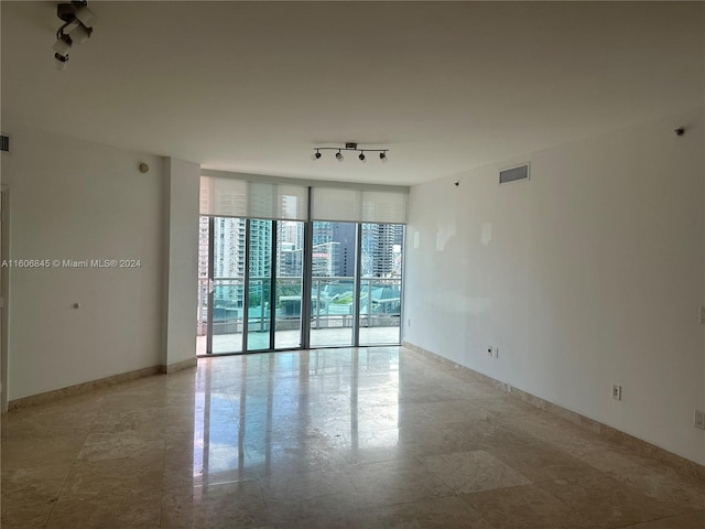 empty room featuring a wall of windows, visible vents, and rail lighting