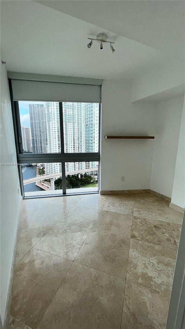 unfurnished room with floor to ceiling windows, tile floors, and rail lighting