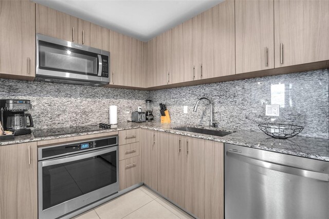 kitchen with light brown cabinetry, sink, light tile patterned flooring, and stainless steel appliances