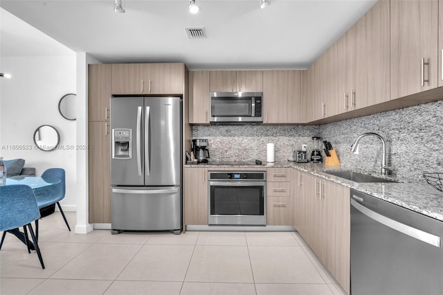 kitchen with sink, light tile patterned floors, light stone countertops, light brown cabinetry, and stainless steel appliances