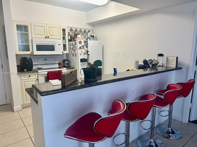 kitchen featuring a breakfast bar area, kitchen peninsula, light tile patterned floors, and white appliances