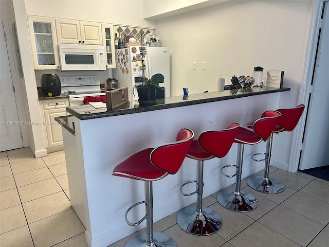 kitchen with white cabinets, a kitchen breakfast bar, white appliances, and kitchen peninsula