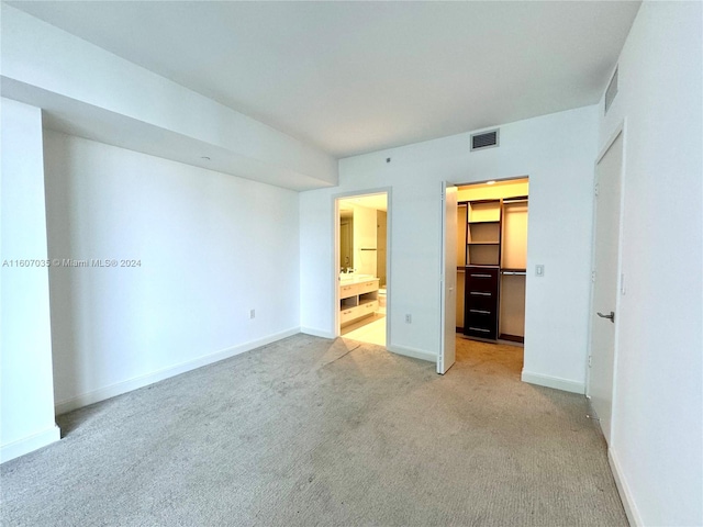 unfurnished bedroom with a closet, a spacious closet, light colored carpet, and ensuite bathroom