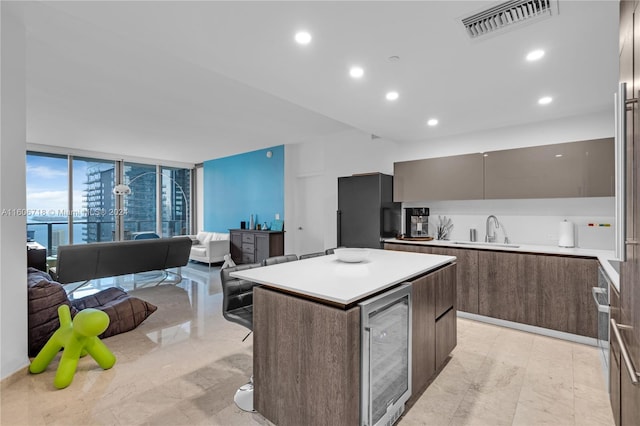 kitchen with black fridge, a kitchen island, beverage cooler, a wall of windows, and sink