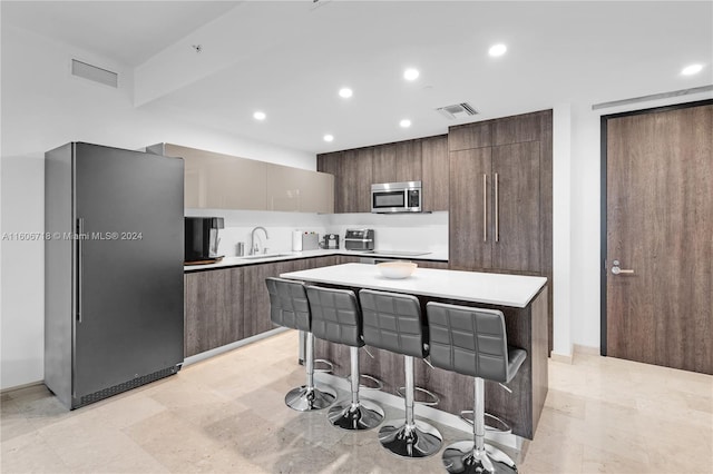 kitchen featuring stainless steel appliances, a center island, sink, light tile floors, and a breakfast bar