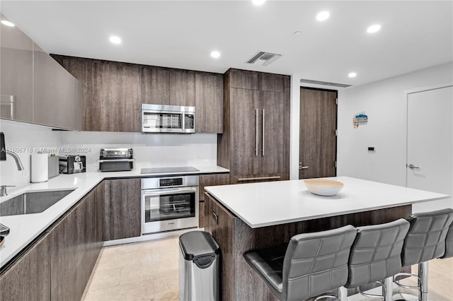 kitchen with sink, a kitchen breakfast bar, light tile flooring, and stainless steel appliances