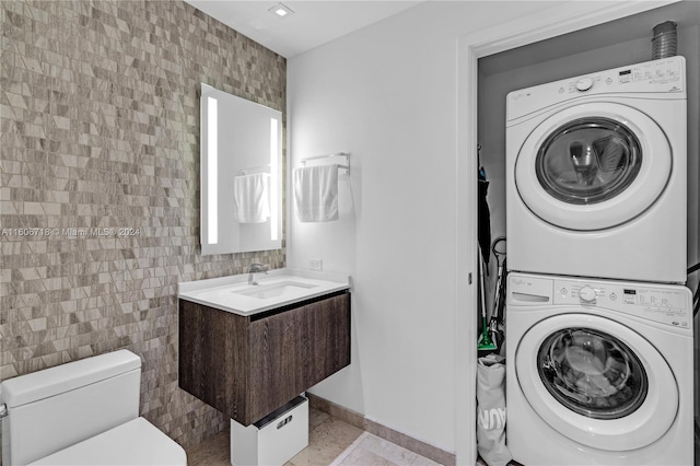 clothes washing area featuring stacked washer / dryer, sink, tile walls, and light tile floors