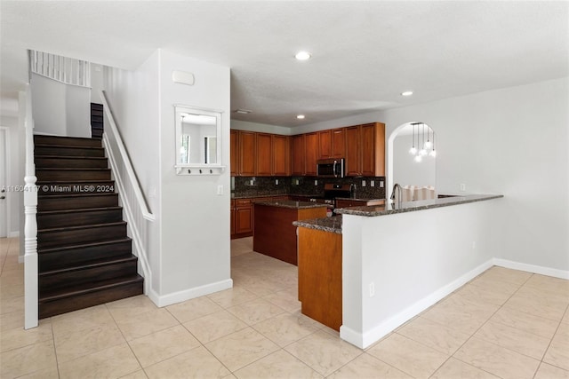 kitchen with decorative backsplash, appliances with stainless steel finishes, kitchen peninsula, sink, and dark stone countertops