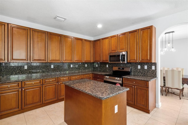 kitchen with decorative backsplash, dark stone counters, stainless steel appliances, a center island, and hanging light fixtures