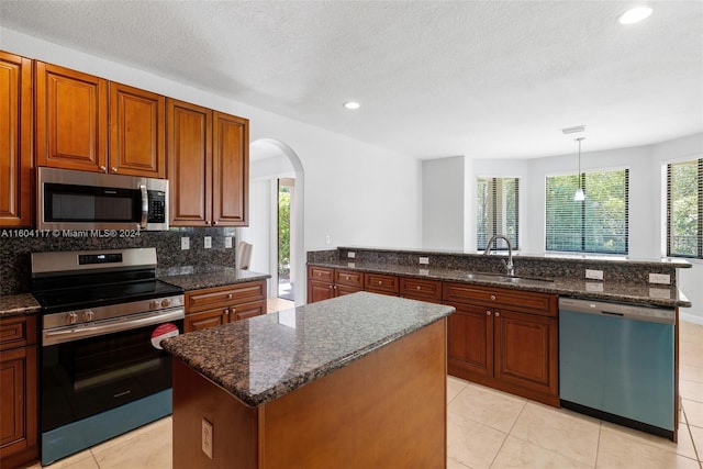 kitchen with sink, hanging light fixtures, stainless steel appliances, a textured ceiling, and a kitchen island