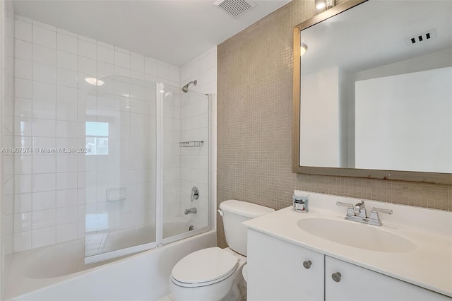 full bathroom with bath / shower combo with glass door, tile walls, vanity, and toilet