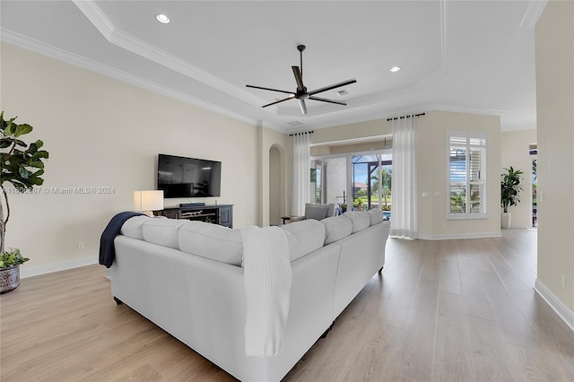 living room with light hardwood / wood-style flooring, ornamental molding, a raised ceiling, and ceiling fan