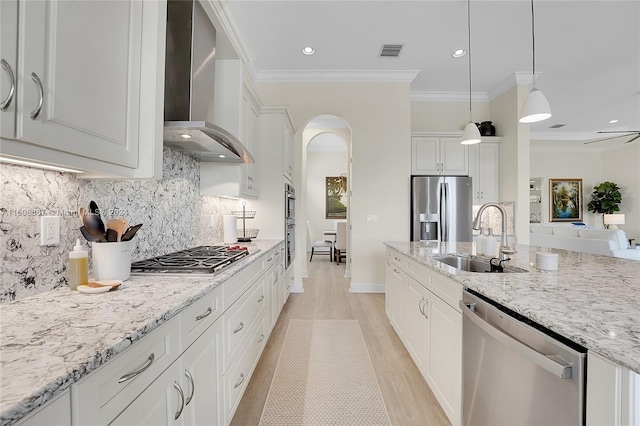 kitchen featuring wall chimney exhaust hood, sink, white cabinetry, hanging light fixtures, and appliances with stainless steel finishes