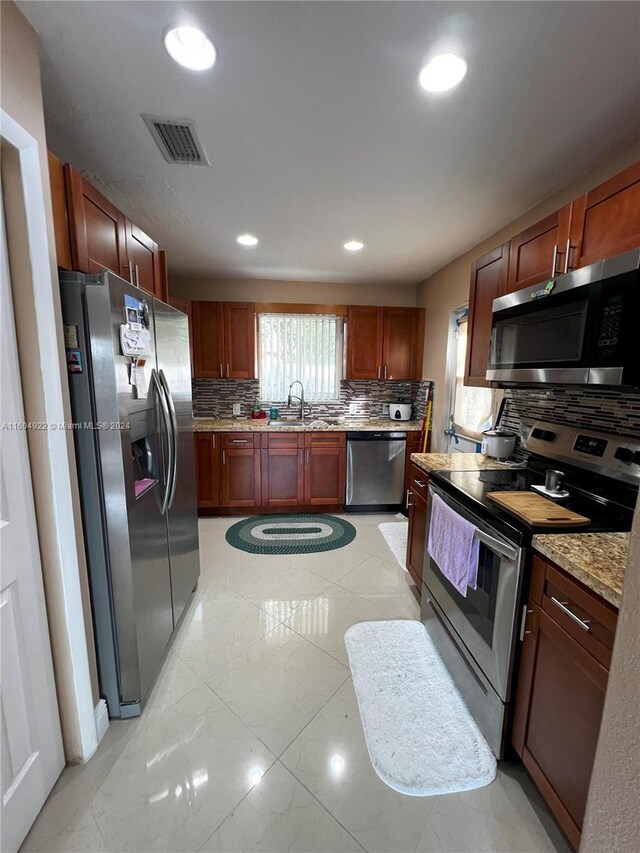 kitchen featuring stainless steel appliances, light stone counters, backsplash, light tile floors, and sink