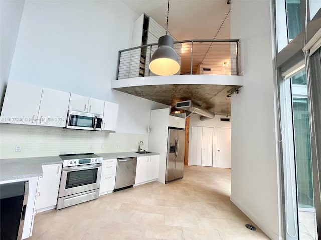 kitchen with white cabinets, sink, a towering ceiling, appliances with stainless steel finishes, and tasteful backsplash