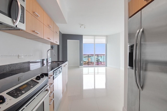 kitchen with dark stone counters, modern cabinets, appliances with stainless steel finishes, expansive windows, and a sink