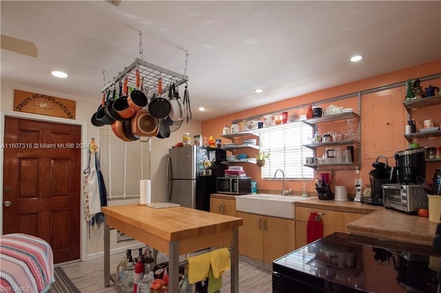 kitchen featuring a toaster, tile countertops, stainless steel appliances, open shelves, and a sink