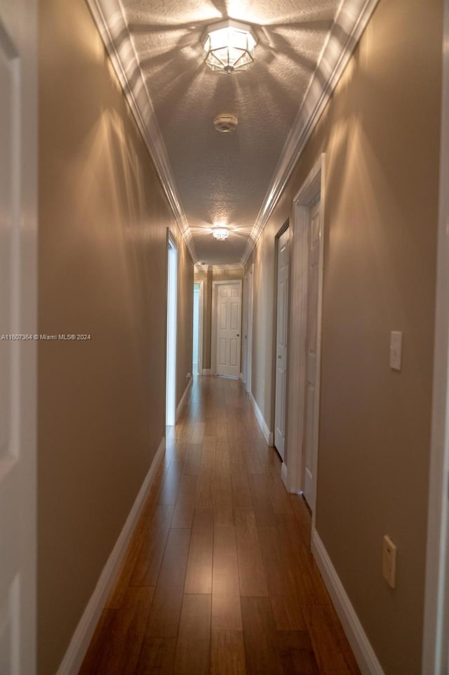 corridor with wood-type flooring, ornamental molding, and a textured ceiling