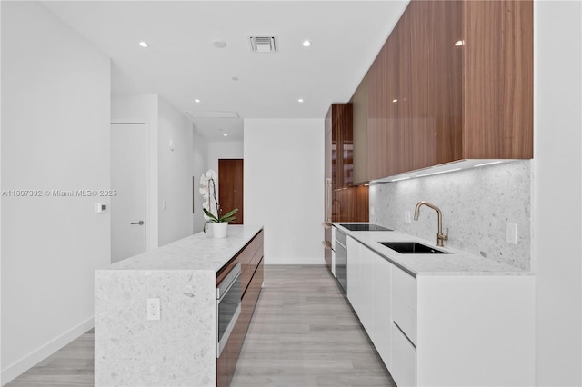 kitchen featuring sink, a center island, tasteful backsplash, white cabinets, and light wood-type flooring