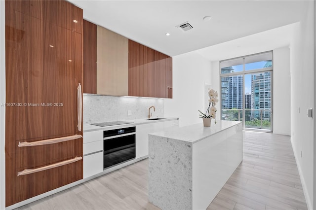 kitchen with sink, a wall of windows, tasteful backsplash, black appliances, and a kitchen island